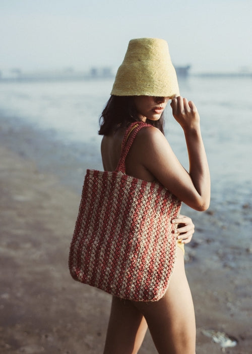 Woman on a beach holding a woven bag and straw hat