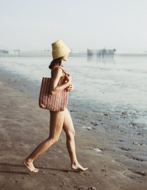 Woman walking on a beach with a yellow hat and patterned bag