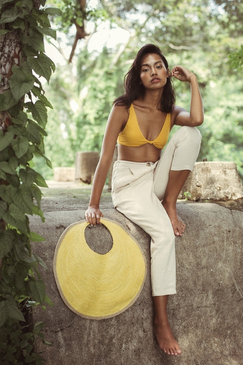 Woman in yellow top and white pants holding a yellow circular object in a natural setting