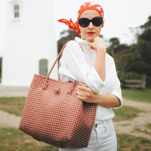 Woman holding a woven brown bag outdoors with a blurred background
