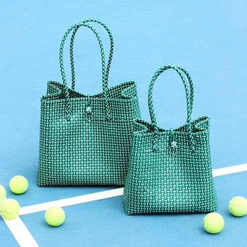 Two green woven bags on a blue surface with tennis balls around them.