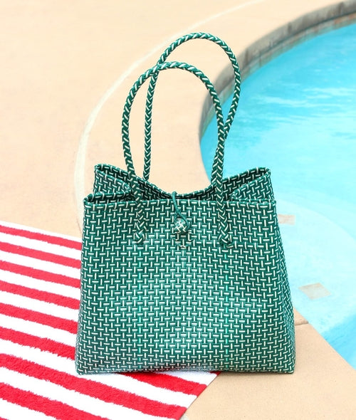 Green woven handbag on a striped towel by a pool