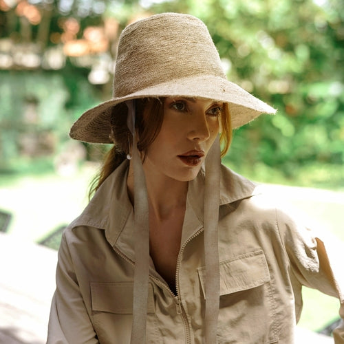 Woman wearing a beige hat and matching jacket outdoors with greenery in the background