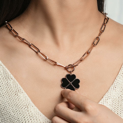 Rose gold chain necklace with a black clover pendant on a person wearing a white top.