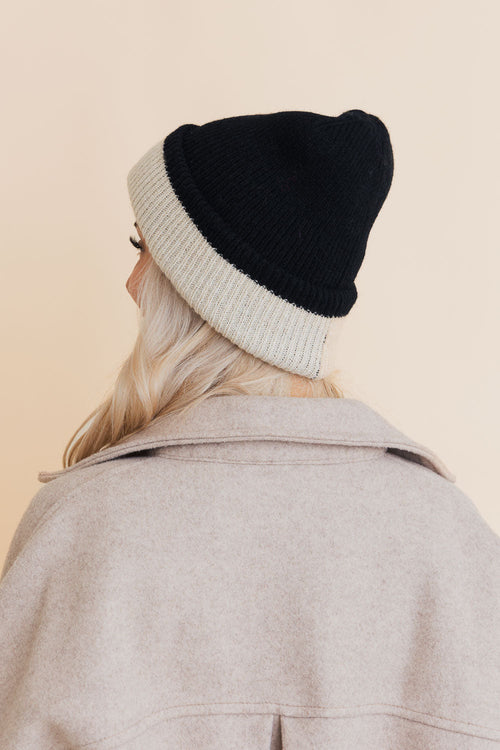 Person wearing a two-tone beanie and coat on a beige background