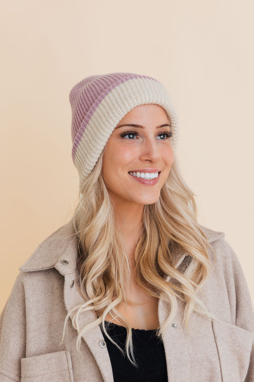 Woman wearing a two-tone beanie and beige coat on a beige background