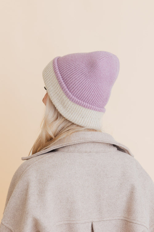 Person wearing a two-tone beanie with purple top and white bottom on a beige background