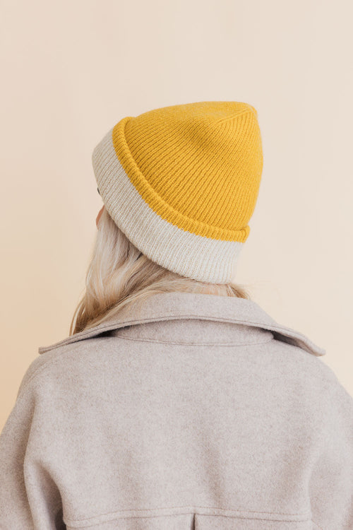 Person wearing a two-tone beanie with yellow top and gray bottom on a beige background
