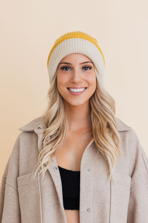 Woman wearing a beige coat and yellow knit beanie against a beige background