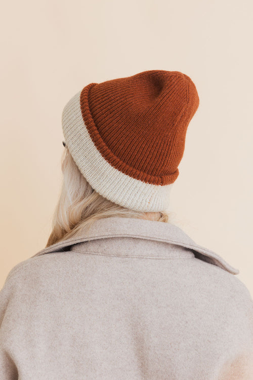 Person wearing a two-tone beanie with rust and gray on a beige background