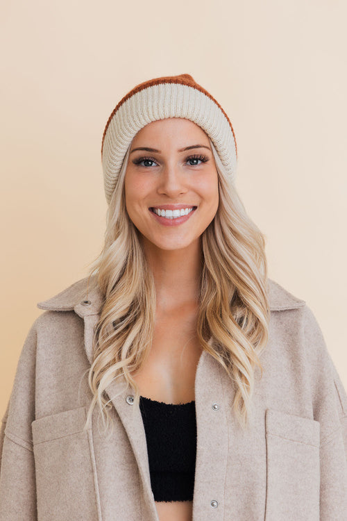 Woman wearing a beige beanie and coat on a beige background
