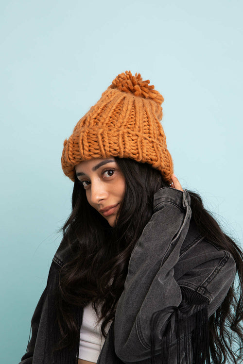 Person wearing a knitted orange beanie against a light blue background