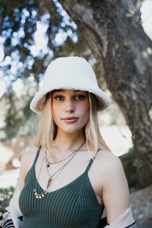 Woman wearing a white fur hat and green top outdoors with trees in the background