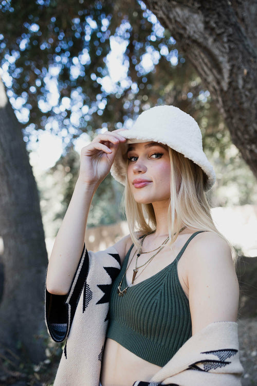 Woman wearing a green bikini top and white hat outdoors with trees in the background