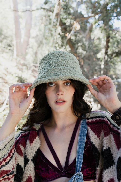 Woman wearing a patterned cardigan and denim overalls in a forest setting