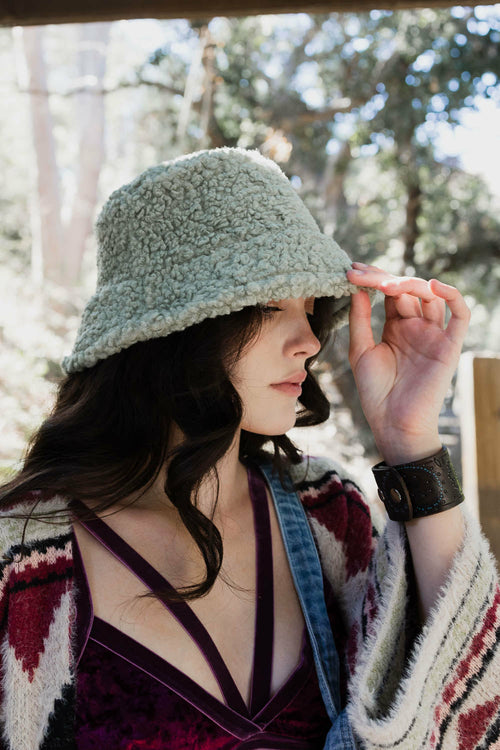 Woman wearing a textured green hat outdoors with trees in the background