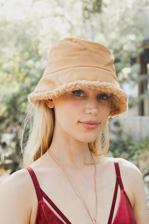 Woman wearing a beige bucket hat with a blurred outdoor background