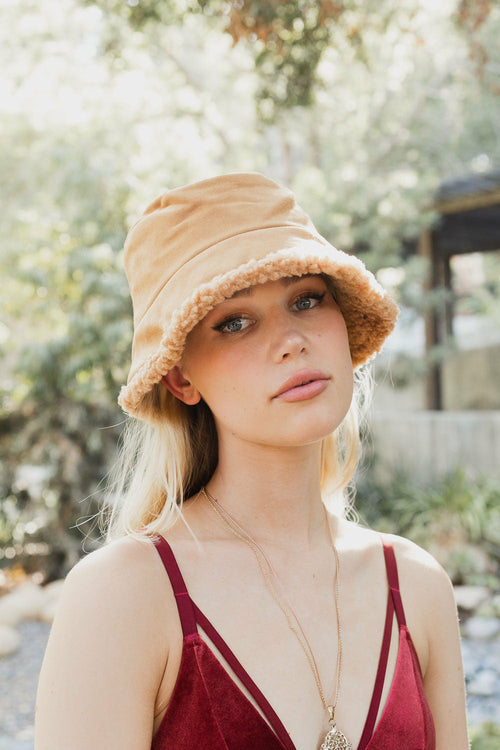 Woman wearing a beige bucket hat and red top outdoors with blurred background