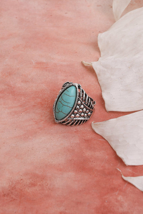 Silver ring with a turquoise stone on a pink surface with white petals