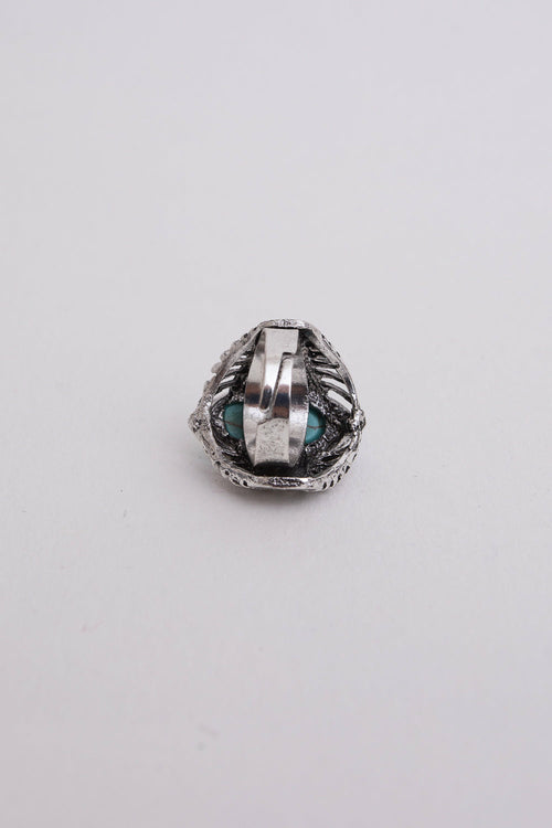 Silver ring with a textured band and blue gemstone on a light gray background