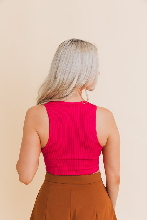 Person wearing a bright pink sleeveless top and brown pants on a beige background