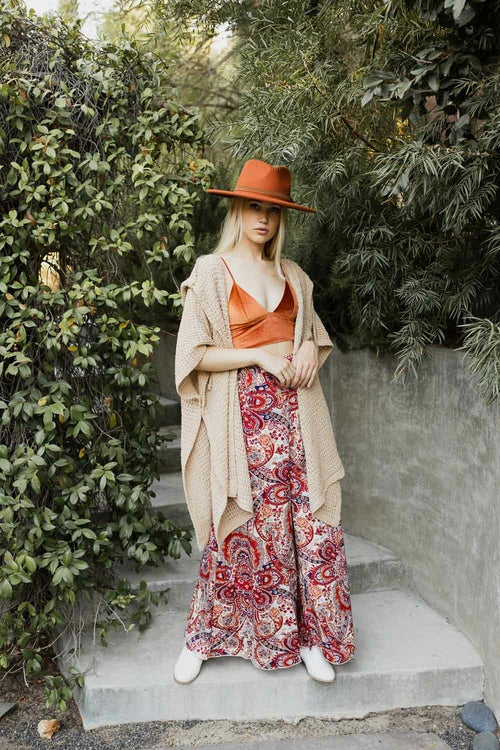 Woman in a stylish outfit with a hat, cardigan, and patterned pants standing outdoors.