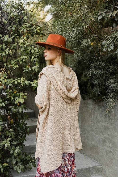 Woman wearing a beige knitted cardigan and red hat standing in a garden.