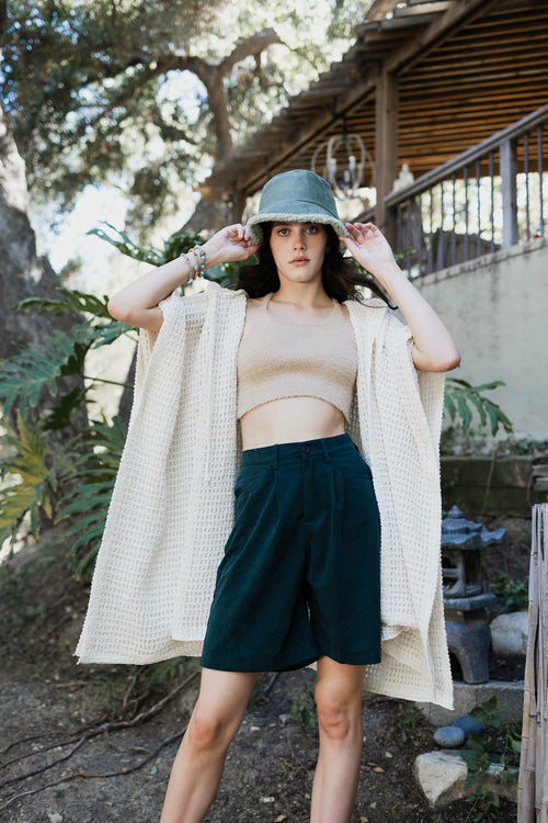 Woman wearing a beige cardigan, beige top, and green shorts outdoors.