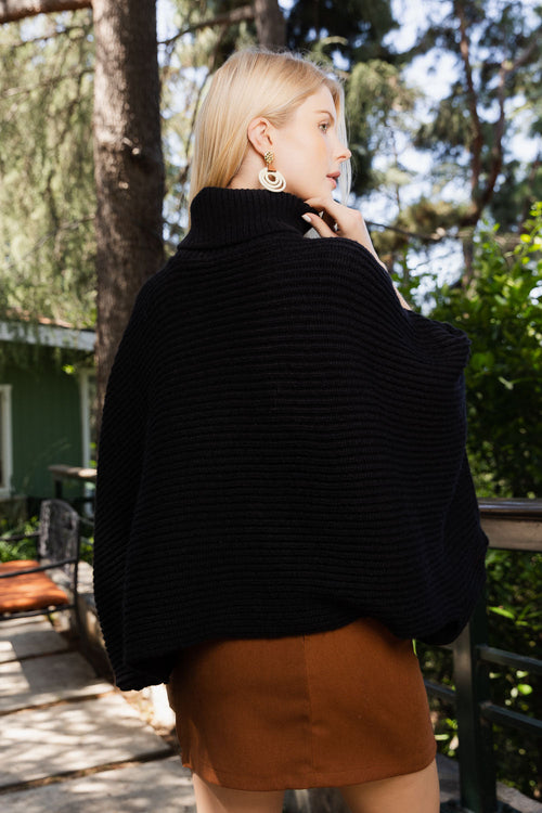 Woman wearing a black sweater and brown skirt outdoors with trees and a building in the background
