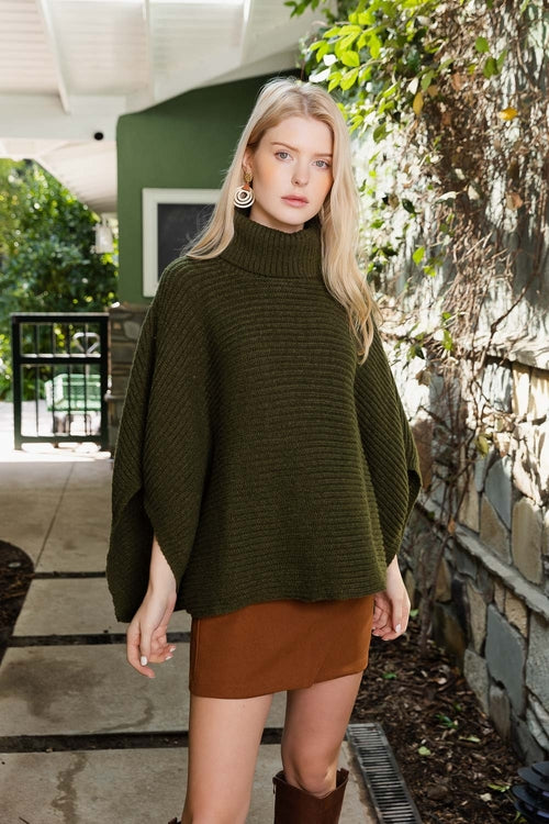Woman wearing a green sweater and brown skirt standing outdoors near a stone wall.