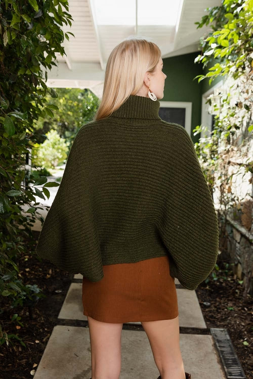 Person wearing a green poncho and brown skirt standing outdoors.