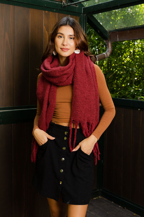 Woman wearing a red scarf and black skirt standing against a wooden wall.