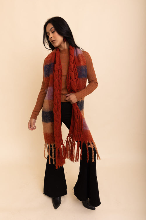 Woman wearing a long, patterned scarf with fringes on a beige background
