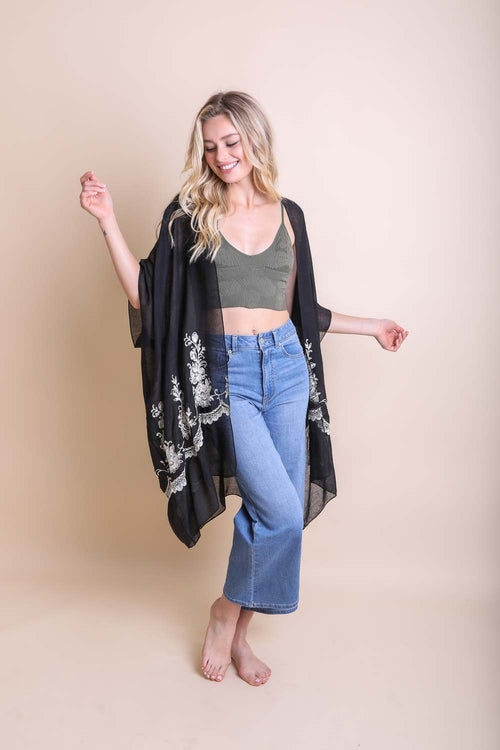 Woman wearing a black floral kimono over a green top and blue jeans on a beige background