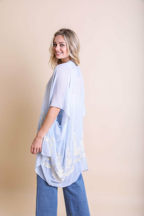 Woman wearing a light blue kimono-style garment with floral patterns on a beige background