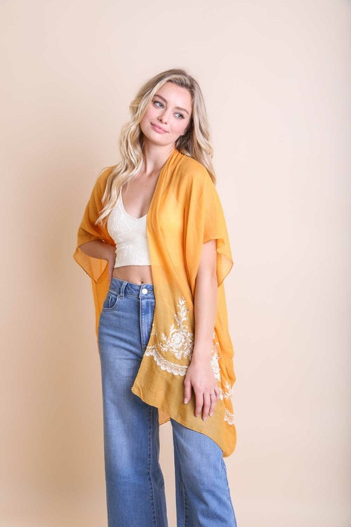 Woman wearing an orange kimono-style garment over a white top and blue jeans on a beige background