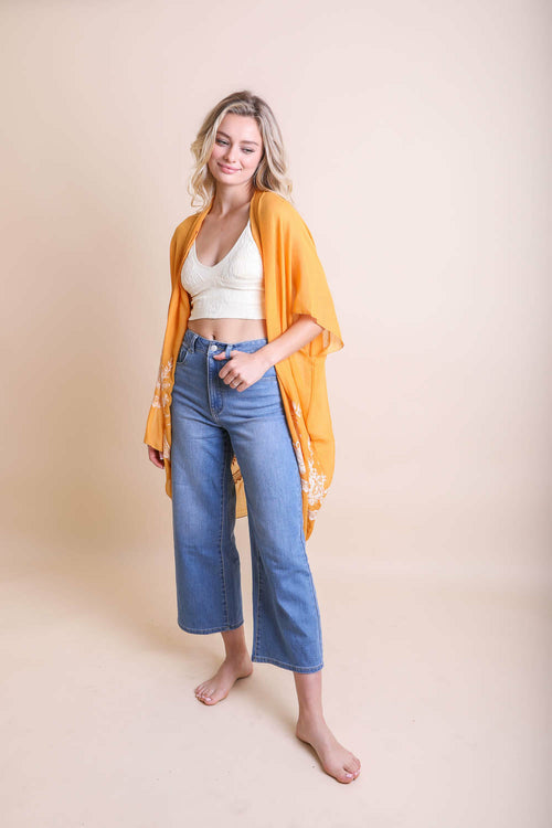 Woman wearing a yellow cardigan, white top, and blue jeans on a beige background