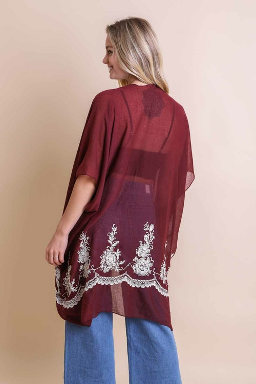 Woman wearing a burgundy embroidered kimono with blue pants on a beige background