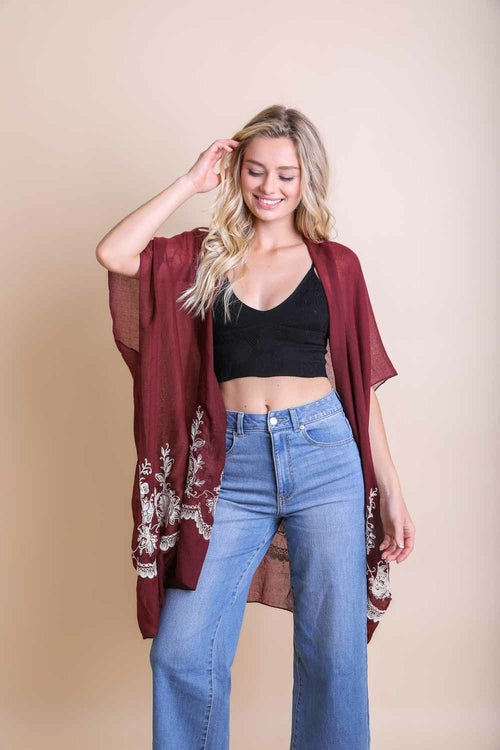 Woman wearing a burgundy kimono, black top, and blue jeans on a beige background