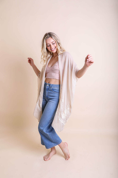 Woman wearing a beige cardigan, pink top, and blue jeans against a beige background