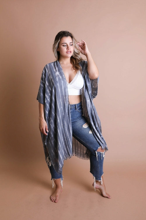 Woman wearing a kimono-style garment over a white top and blue jeans on a beige background