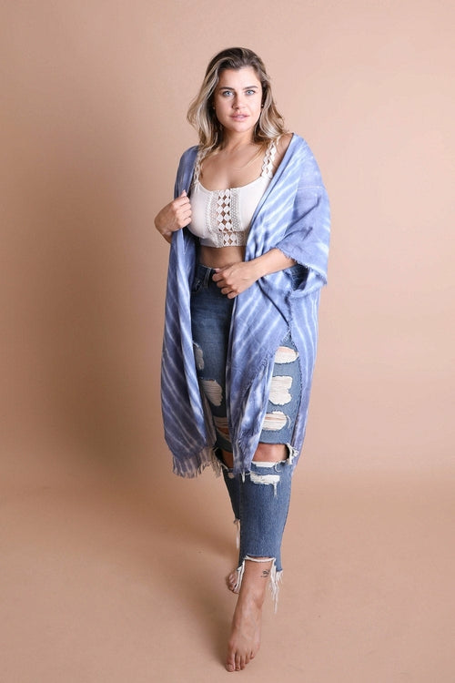 Woman wearing a blue kimono-style garment over a white top and ripped jeans on a beige background