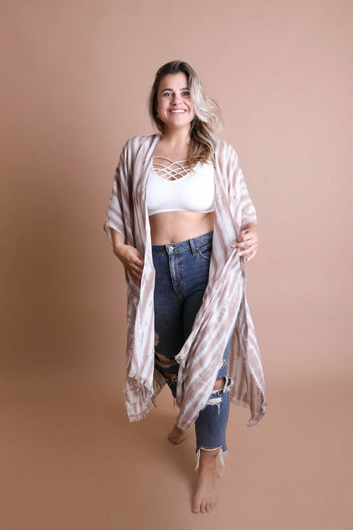 Woman wearing a long, light-colored kimono over a white top and blue jeans on a beige background