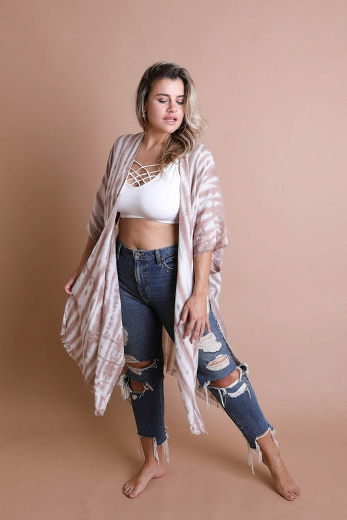 Woman wearing a patterned kimono over a white top and ripped jeans on a beige background
