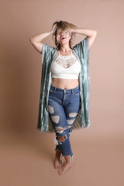 Woman wearing a green kimono over a white top and blue jeans on a beige background