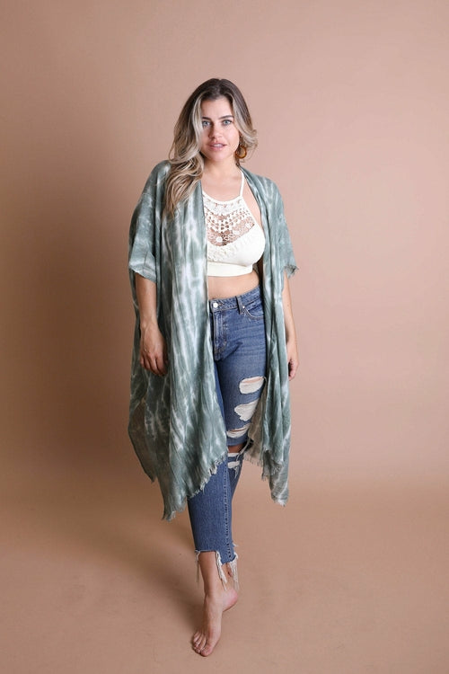 Woman wearing a green kimono-style garment over a white top and blue jeans on a beige background