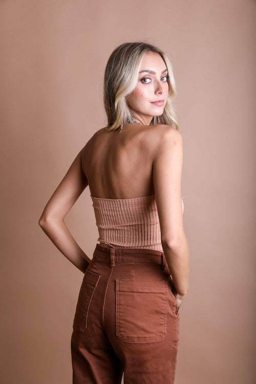Woman wearing a beige top and brown pants against a beige background
