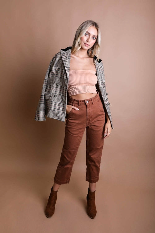 Woman wearing a plaid jacket, pink top, and brown pants against a beige background