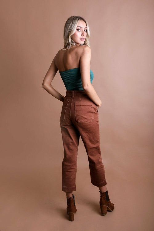 Woman wearing a teal top and brown pants against a beige background