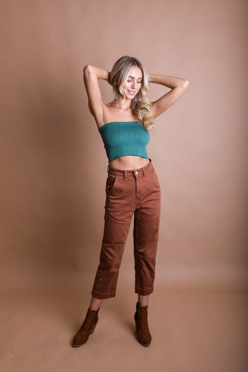 Woman wearing a teal top and brown pants against a beige background